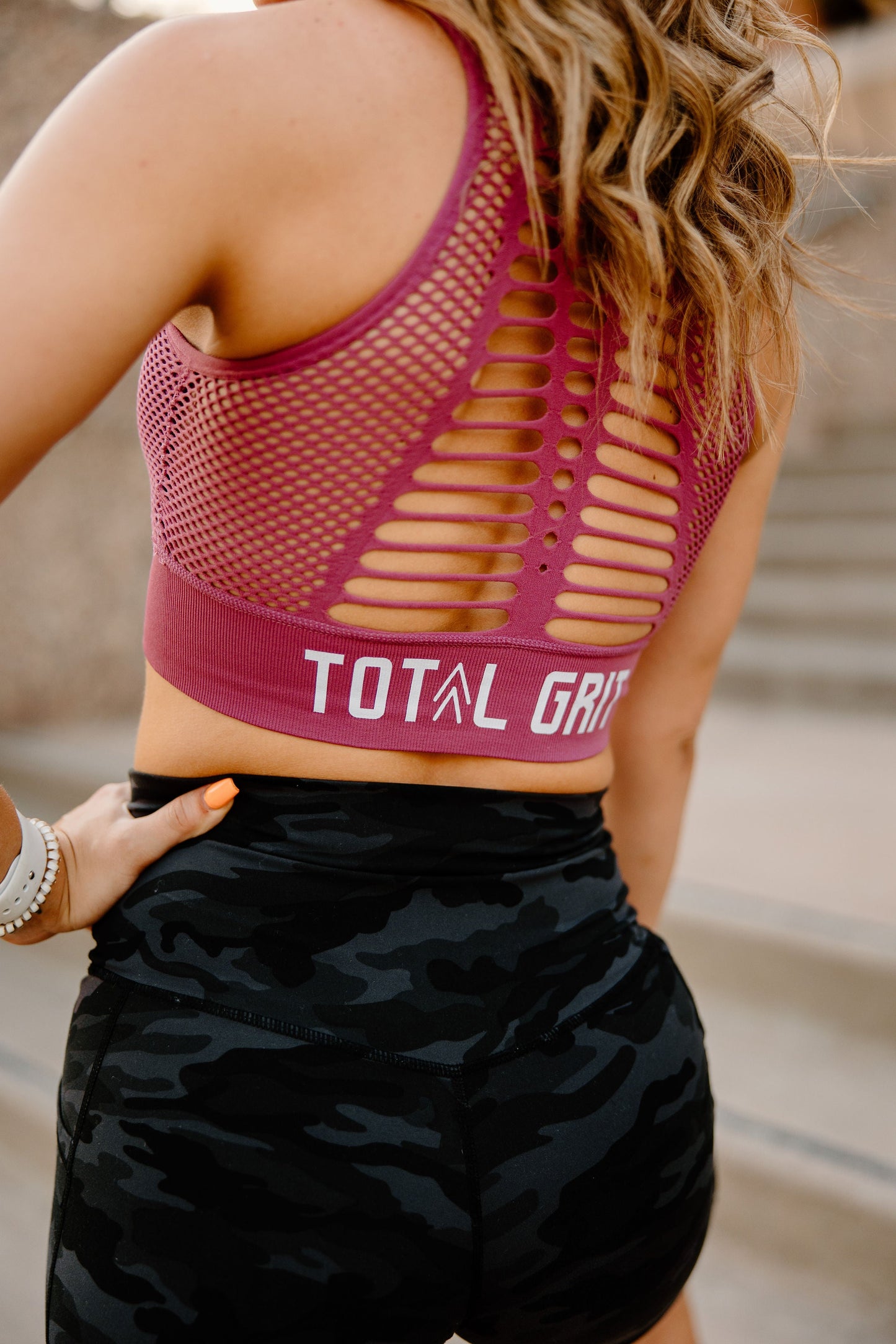 Backside view of the vibrant pink Total Grit sports bra. Breathable webbing on the backside, and white Total Grit logo.