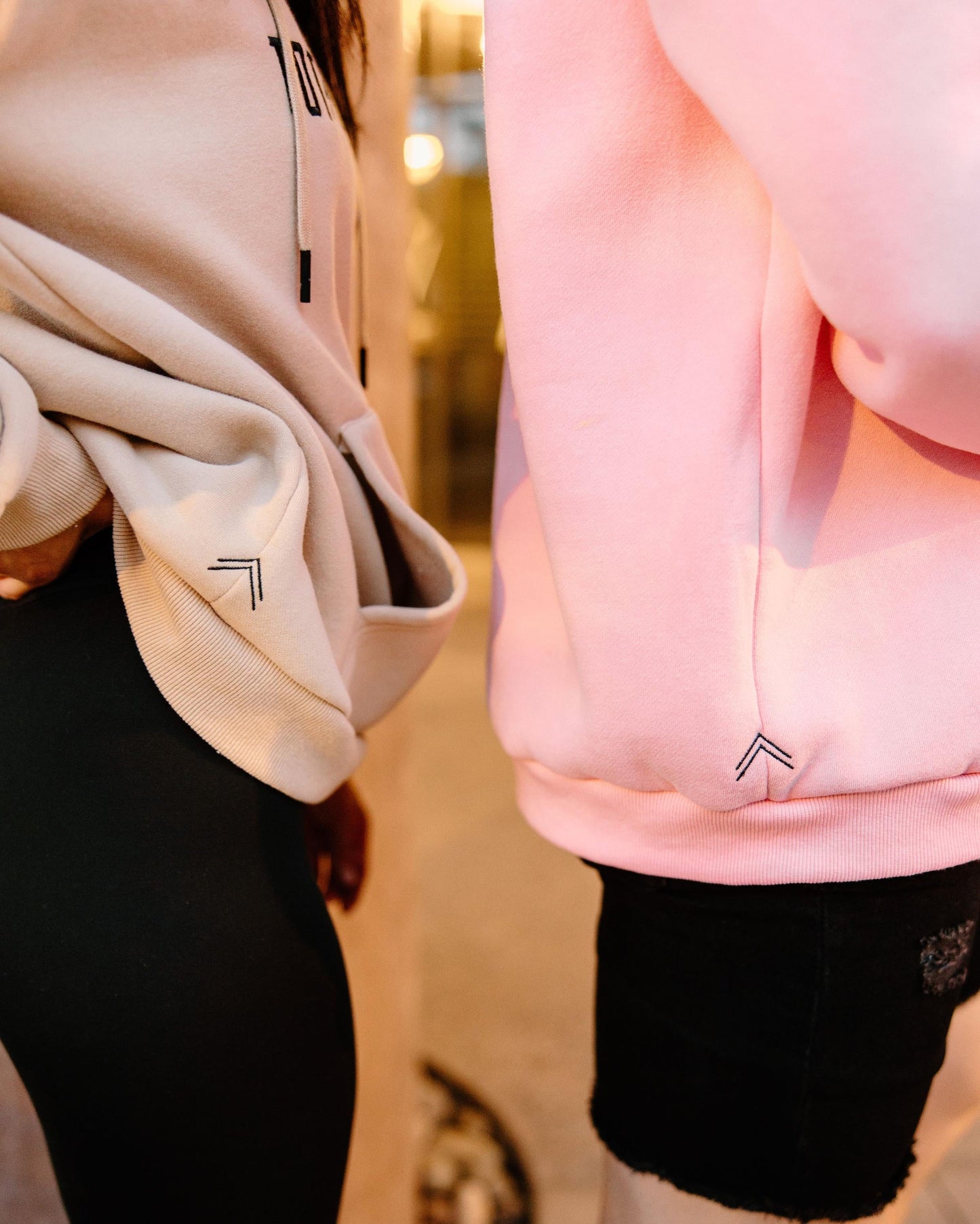 Close up detailed shot of the Pastel Hoodies in Khaki & Pink. Showing off the side profile of the double caret logo ^^ meaning "Create Your Own Reality".