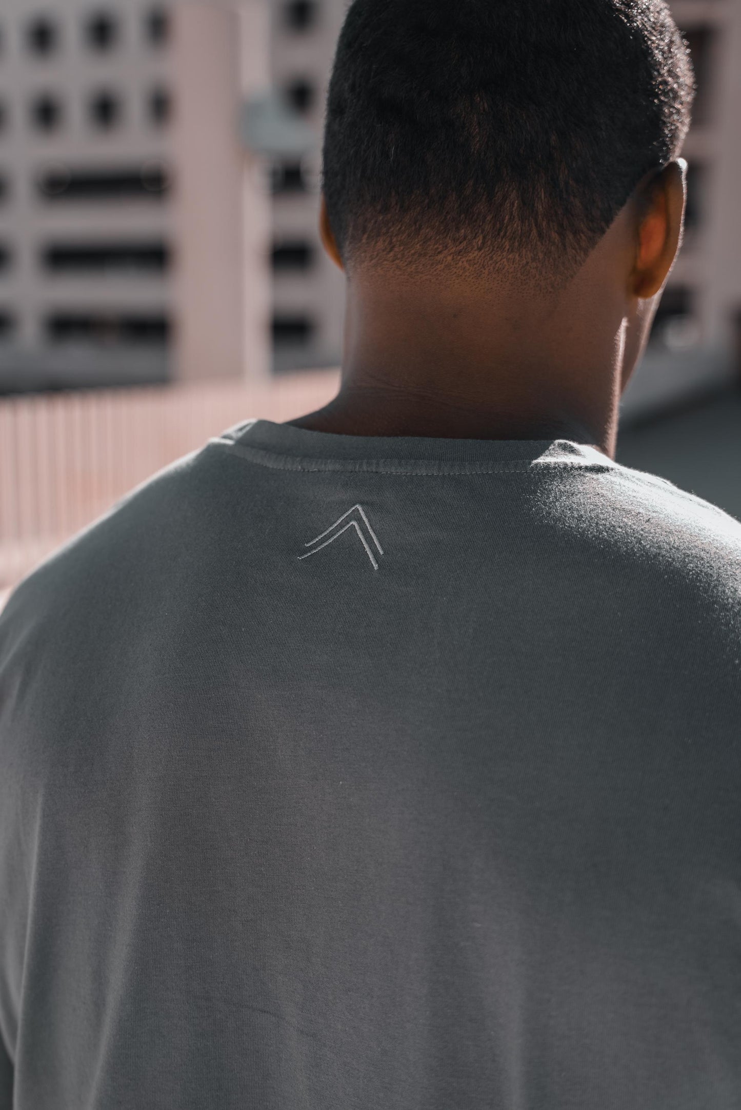 Close up shot of the back of the grey long sleeve, showing the double caret logo ^^ meaning "Create Your Own Reality"