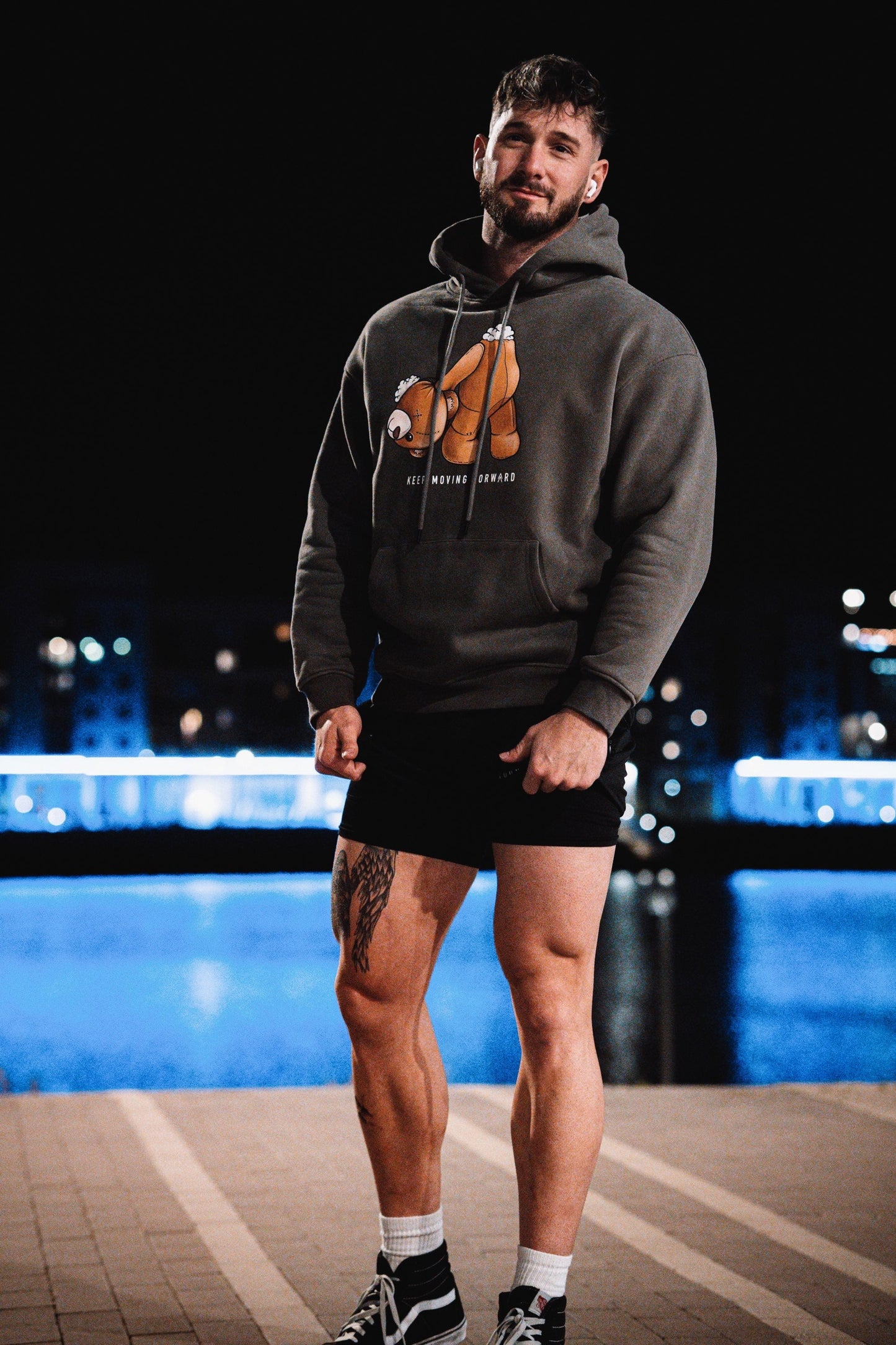 Male model cheesing in our grey Keep Moving Forward hoodie, showing our teddy in shambles, but still keeping their head about them.